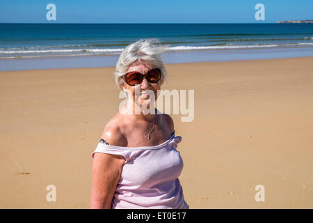 Eine Dame zu Fuß auf einem leeren Strand trägt ein pinkes Top und eine Sonnenbrille auf. Stockfoto