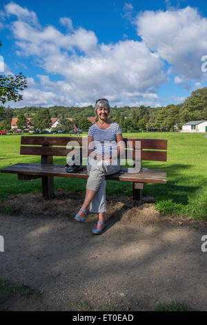 Eine Frau saß auf einer Bank im Park genießen Sie den herrlichen Sonnenschein Stockfoto