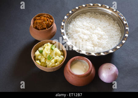 Indischer Pakhala-Reis zum Mittagessen in einer Stahlschüssel und pikante Gurkenstampfkartoffeln mit Chilis, Joghurt auf erdfarbenem Topf, Zwiebeln, schwarzem Hintergrund Stockfoto