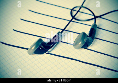 ein paar Kopfhörer platziert auf einem Stab gezeichnet auf einem Notizblock Simulation von Musiknoten, mit einer leichten Vignette hinzugefügt Stockfoto