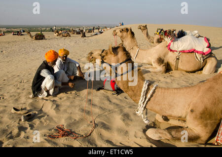 Männer und Kamel sitzen auf Sand Düne wartet auf Touristen Safari in Khuri in Jaisalmer, Rajasthan Indien Asien Stockfoto