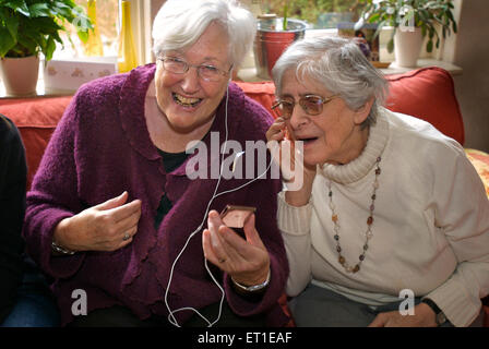 Zwei ältere Frauen, die gemeinsam Musik hören von einem i-Pod mit Kopfhörer zum ersten Mal in ihrem Leben Stockfoto