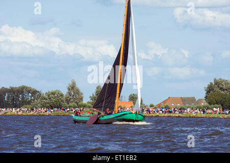 Eine historische Flachboden-Boot segelt auf einem der Seen in Friesland mit Zuschauern Skutsjesilen in Holland Stockfoto