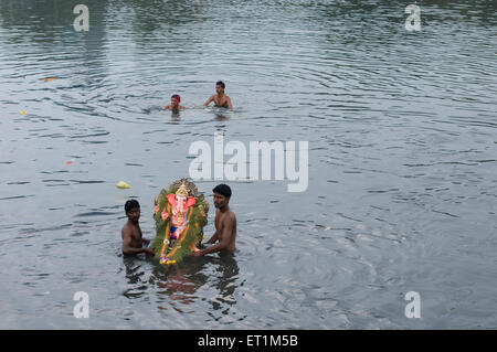 Ein kleines Idol von Lord Ganesh ergriffen durch zwei MannSchönheitschirurgie Untertauchen im Wasser Pune Indien Asien Stockfoto