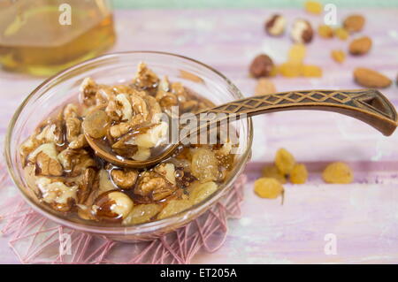 Walnüsse, Haselnüsse und Honig in eine Glasschale mit einem Vintage Holzlöffel auf einem rosa Tischdecke Stockfoto