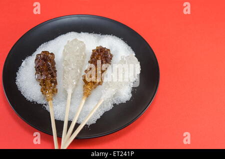 Zwei Zuckersticks mit weißen und braunen Zucker in einem schwarzen Teller vor einem roten Hintergrund Stockfoto