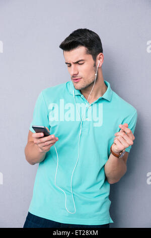 Lässige jungen Mann halten Smartphone und hören von Musik im Kopfhörer über grauen Hintergrund Stockfoto