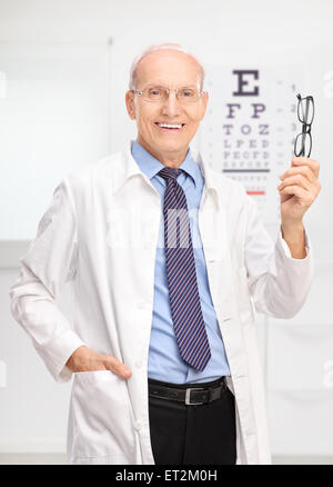 Vertikale Schuss ein Reifen Optiker Brille hält und posieren in seinem Büro vor ein Auge Tabelle Stockfoto