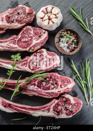 Rohe Lammkoteletts mit Knoblauch und Kräutern auf dem alten Holztisch. Stockfoto