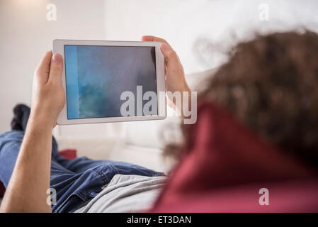 Mann auf der Couch liegend und mit Hilfe einer digitalen-Tablets, München, Bayern, Deutschland Stockfoto