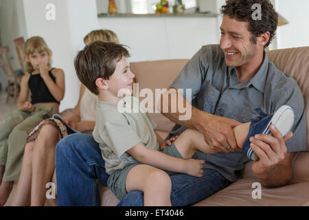 Familie mit zwei Kindern auf einer Couch, Vater Sohn Schuhe anziehen Stockfoto