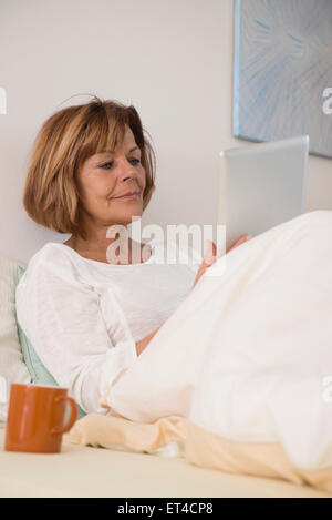 Ältere Frau am Bett sitzen und mit einer digital-Tablette, München, Bayern, Deutschland Stockfoto