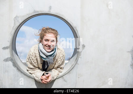 Junge Frau, die durch ein rundes Loch in die Betonwand Bayern München Stockfoto