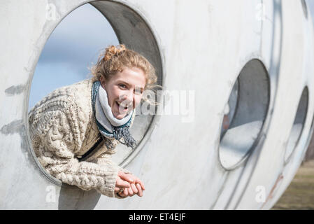 Junge Frau, die durch ein rundes Loch in die Betonwand Bayern München Stockfoto