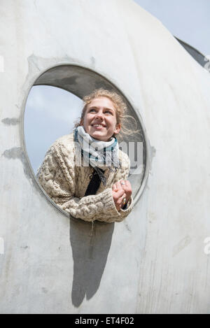 Junge Frau, die durch ein rundes Loch in die Betonwand Bayern München Stockfoto