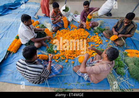 Männer schaffen Blumengirlanden auf dem Boden an Thovalai Flower market Stockfoto