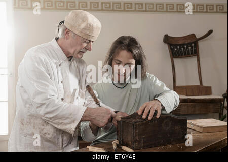 Restaurator Meister erklärt Lehrling etwas auf einem antiken Knochen-Box, Bayern, Deutschland Stockfoto