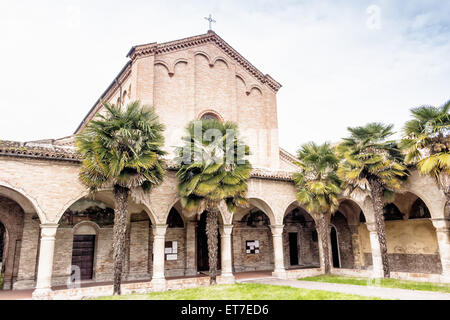 Brickwall Fassade und Kolonnade mit Bögen der XV Jahrhundert römische gotische Kirche Saint Francis in Cotignola in der Nähe von Ravenna in der Landschaft der Emilia Romagna in Italien gewidmet. Reihen von Palmen säumen den Garten. Stockfoto