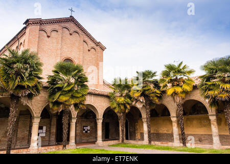 Brickwall Fassade und Kolonnade mit Bögen der XV Jahrhundert römische gotische Kirche Saint Francis in Cotignola in der Nähe von Ravenna in der Landschaft der Emilia Romagna in Italien gewidmet. Reihen von Palmen säumen den Garten. Stockfoto