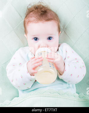 Süßes kleines Baby mit schönen blauen Augen Trinkmilch in einer Plastikflasche entspannend auf einer blauen gestrickte Decke Stockfoto