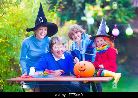 Glückliche Familie, Eltern mit zwei Kindern tragen Hexe-Kostüm und Hut feiert Halloween und Kürbis schnitzen im Garten Stockfoto