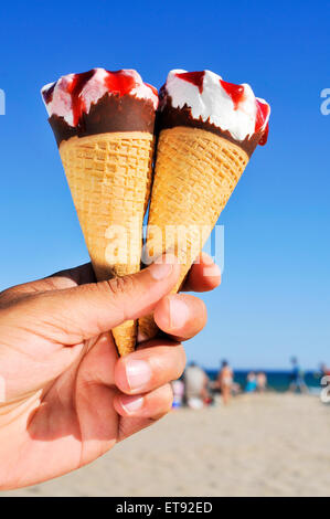 Closeup von einem kaukasischen Jüngling mit einigen Eistüten von verschiedenen Geschmacksrichtungen in der Hand am Strand Stockfoto