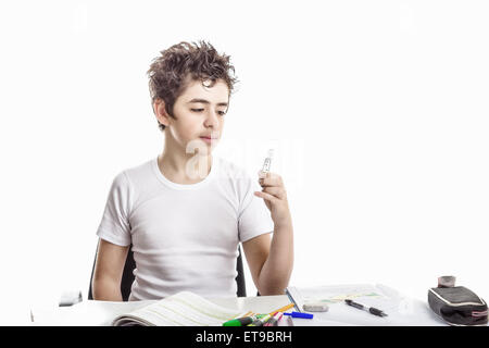 Junge ist Hausaufgaben: sitzen vor einem Schreibtisch von Büchern, Heften und Stiften abgedeckt, er eine Glühbirne mit seiner linken Hand hält und mit der Befragung Augen Uhren Stockfoto