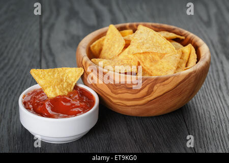 Tortilla-chips in Oliven Holz Schüssel mit Tomatensauce auf Holztisch Stockfoto