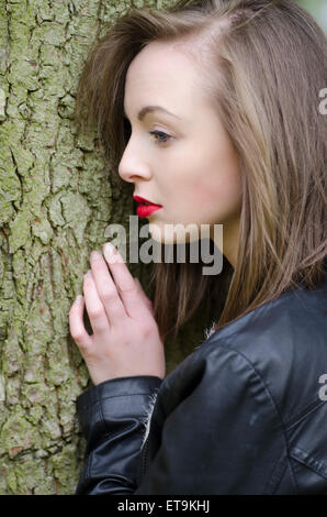 Schöne junge Frau, die sich hinter einem Baum versteckt Stockfoto