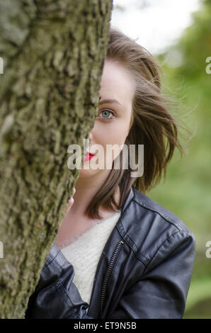 Junge Frau, die sich hinter einem Baum versteckt Stockfoto