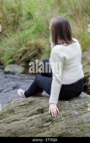 Junge Frau setzte sich auf den Felsen Stockfoto