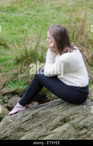 Junge Frau setzte sich auf den Felsen Stockfoto