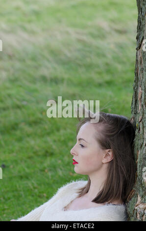 Ernste junge Frau lehnt sich an einen Baum wegschauen Stockfoto