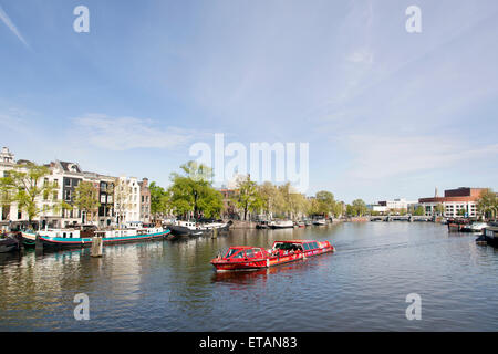roten Grachtenboot auf Fluss Amstel in Amsterdam mit Opernhaus im Hintergrund Stockfoto