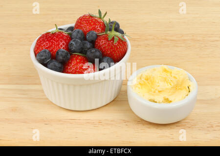 Erdbeeren und Heidelbeeren mit Clotted Cream in ein Töpfchen auf einem Holzbrett Stockfoto