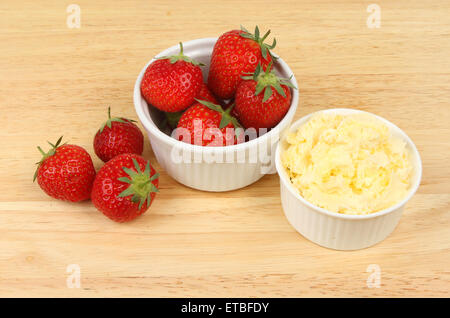 Erdbeeren und Clotted Cream in ein Töpfchen auf einem Holzbrett Stockfoto