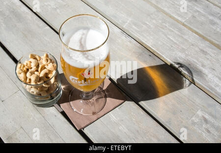 Zwei Bier in dänische Marke Carlsberg-Logo Brille auf rustikalen Holztisch mit Cashew-Nüssen im Freien bei Sonnenschein. Stockfoto