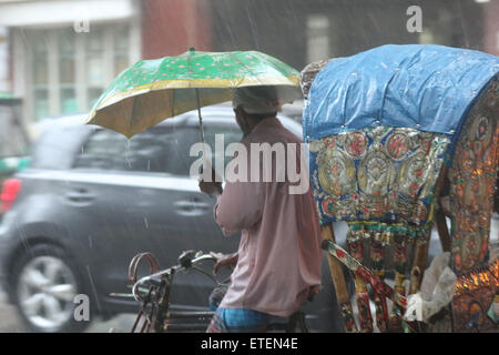 Dhaka, Bangladesch. 13. Juni 2015. Rikscha Abzieher mit Regenschirm bei starkem Regen an der Universität Dhaka, die Stadtbewohner haben in Form von Regen zu entlasten, nachdem er bei heißem Wetter in den letzten Tagen. Stockfoto