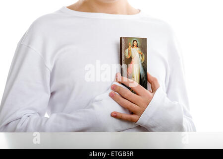 Ein kaukasischen junge hält ruht auf der Brust ein Bild des Barmherzigen Jesus Stockfoto