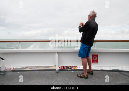 Mann in Shorts und Mohikaner Haarschnitt auf Fähre nimmt Bilder mit Digitalkamera, Ärmelkanal Calais-Dover Stockfoto