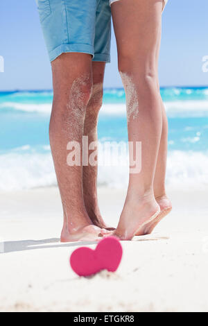 Barfuß weibliche Beine stehen auf Zehenspitzen auf Mannes Füße am Strand mit türkisfarbenem Meer Hintergrund, dekorierte rosa Herz-Objekt.  Rom Stockfoto