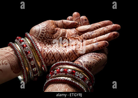 Frau Hände mit Henna halten zwei goldene Hochzeit Ringe auf schwarzem Hintergrund Stockfoto