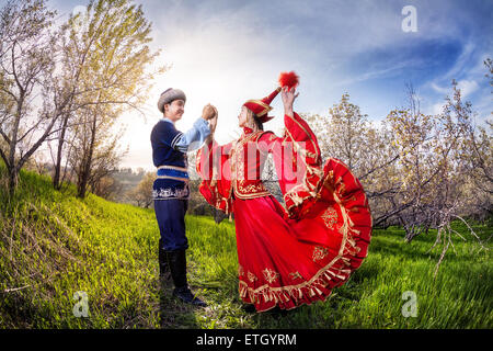 Kasachische Frau tanzt im roten Kleid mit Mann im Frühjahr Apfelgarten in Almaty, Kasachstan, Zentralasien Stockfoto