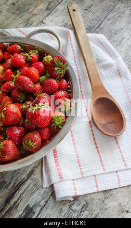Frische Erdbeeren in Metallsieb. In der Nähe von Holzlöffel und Geschirrtuch. Draufsicht Stockfoto