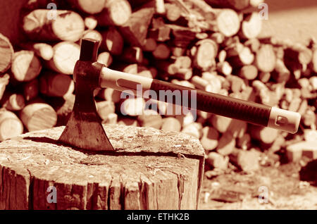 Gelbe Axt mit einem Stück Holz in der Nähe von einem Stapel von Protokollen Stockfoto