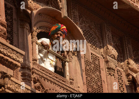 Rajasthani Mann mit Blick vom Fenster in geschnitzten Fassade an Mehrangarh Fort, Jodhpur, Rajasthan, Indien Stockfoto