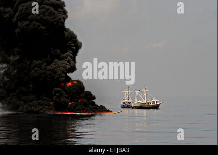 Dunkle Wolken füllen den Himmel wie Krabbenkutter einen Boom verwenden, um Erdöl zu sammeln, während eine kontrollierte Oberfläche brennen nach der BP Deepwater Horizon-Ölkatastrophe als Bemühungen zur Eindämmung und reinigen Sie die Millionen von Gallonen Crew weiter 6. Mai 2010 im Golf von Mexiko. Stockfoto