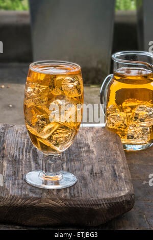 Glas kalte erfrischende Apfelschorle mit Eiswürfeln und Äpfel auf Holztisch Stockfoto