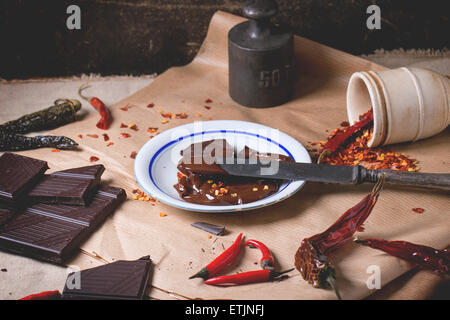 Dunklen Schokolade mit frische und trockene rote scharfe Chilischoten auf Backpapier mit Teller heiße geschmolzene Schokolade und Vintage hacken Stockfoto