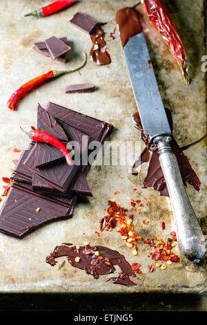 Hacken und schmelzen dunklen Schokolade mit frischen und trockenen red hot Chili Peppers und Vintage Messer in alten Metall-Hintergrund Stockfoto